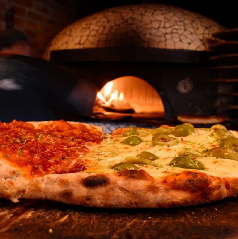 Pizza con aceitunas frente al horno de leña encendido.